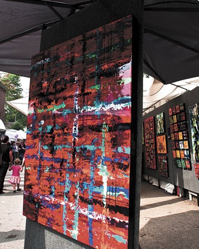 Large abstract red and orange painting hung on an outdoor art show booth under a tent, with more artworks and people in the background.