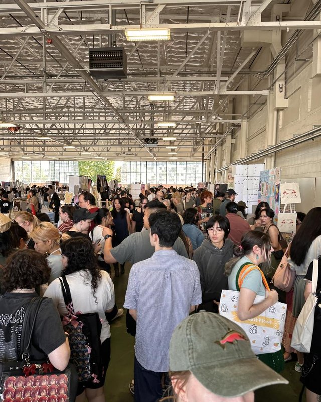 Dense crowd of shoppers browsing inside a large hangar-style market hall.