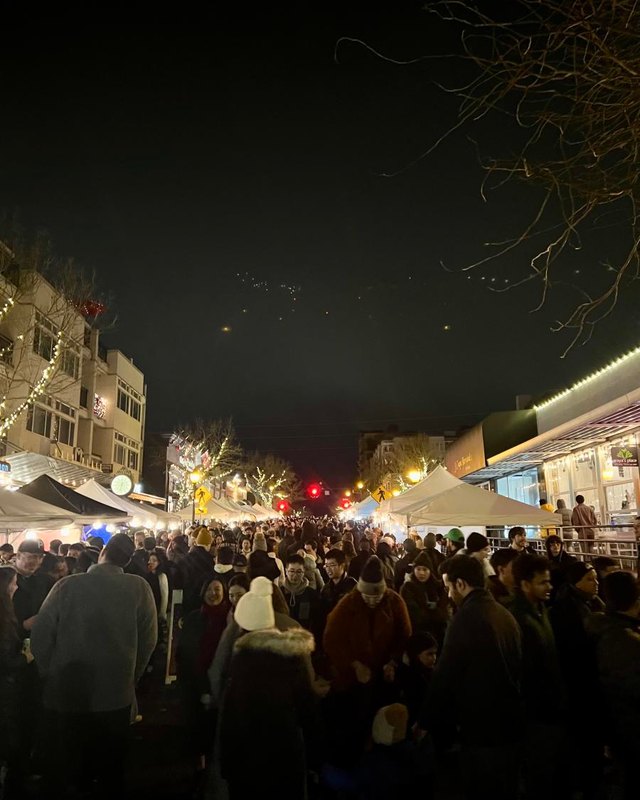 Large crowd of night market visitors walking past lit tents on a city street in Bellevue