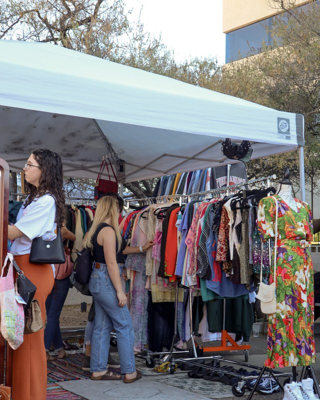 Shoppers browsing clothing racks at an outdoor vintage market tent
