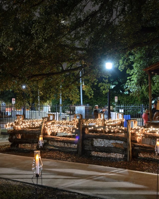 Lit holiday market stalls under oak trees at night in Sam Houston Park