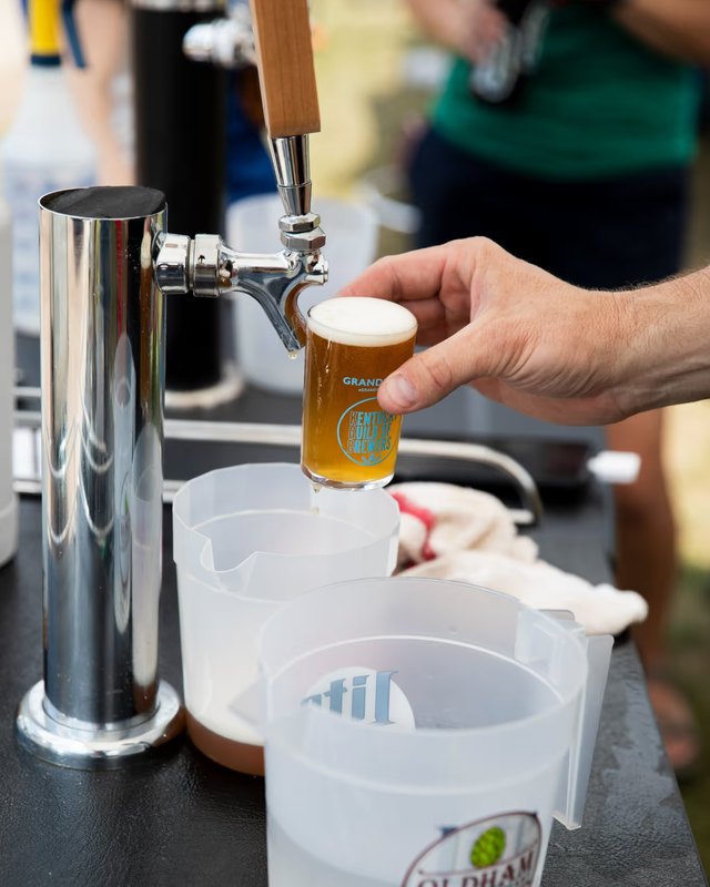 A hand pouring a craft beer from a tap into a plastic cup at a festival booth.