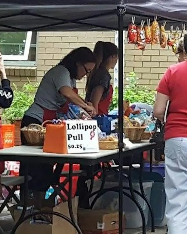 Two vendors behind a tented craft table with a 'Lollipop Pull $0.25' sign at an outdoor fall event; a shopper stands at the right edge.
