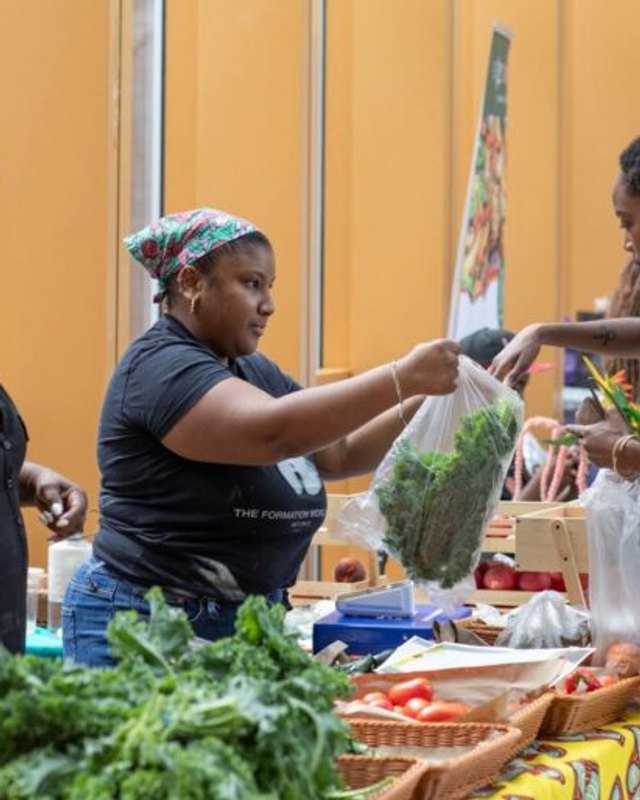 Market vendors handing fresh greens and produce to customers at a Weeksville Green stall.