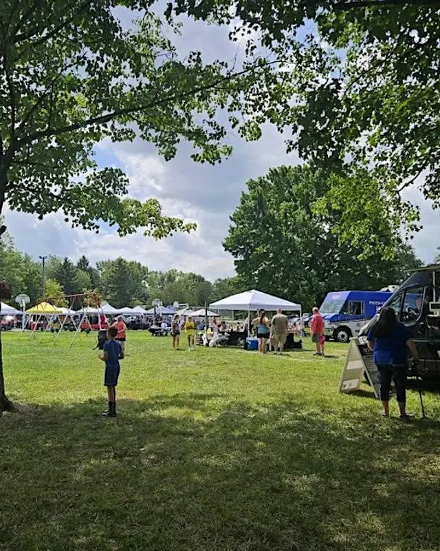 Outdoor park lawn with white vendor tents, a parked truck and people browsing at Beechwood Trails Park.