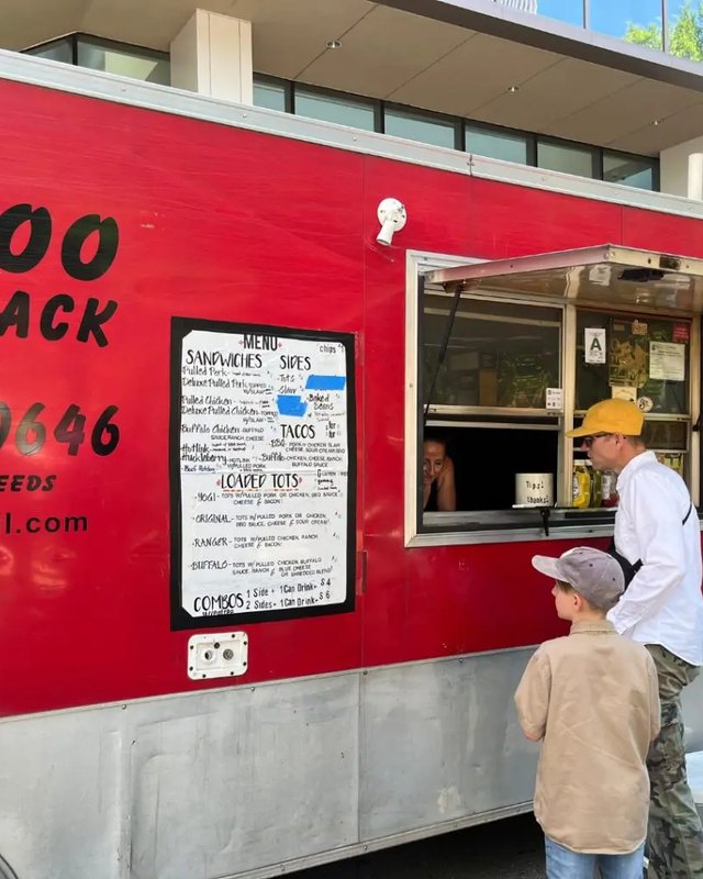 Customer ordering from the serving window of a red Boo Shack food truck on a city street.