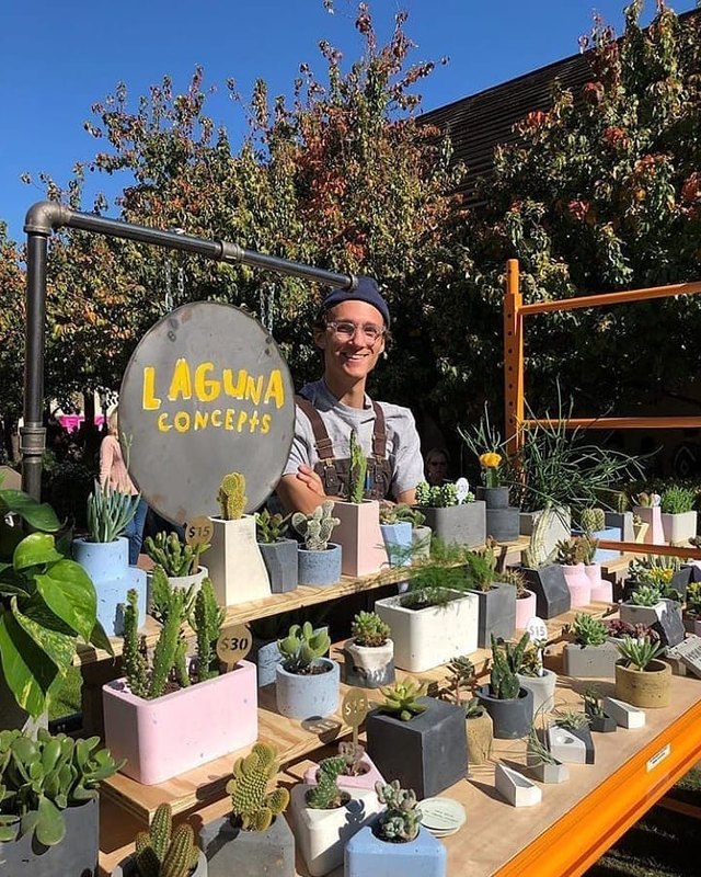Vendor behind a Laguna Concepts booth of potted succulents and cacti at an outdoor market