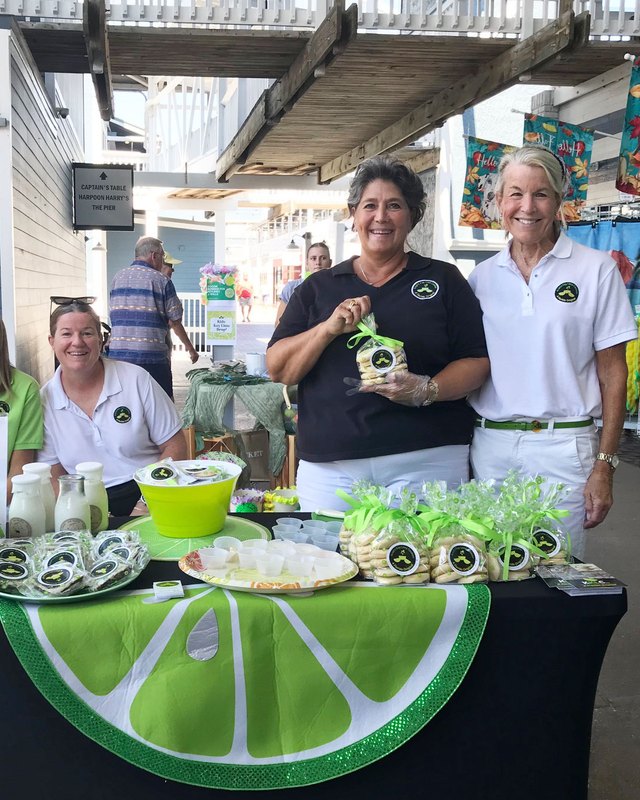 Key lime products and smiling vendors at a booth with a large lime slice tablecloth at the festival.