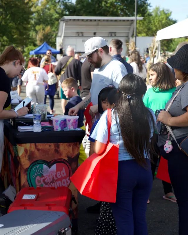 Visitors and families gathered at a festival table with vendor goods at the Bensalem event.