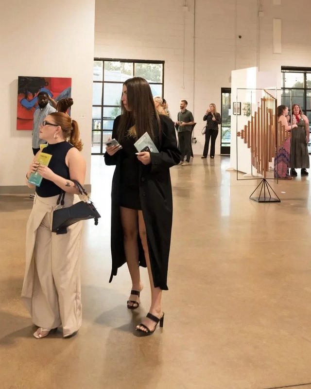 Two visitors holding brochures walk through a bright gallery space during the Texas Vignette art fair.