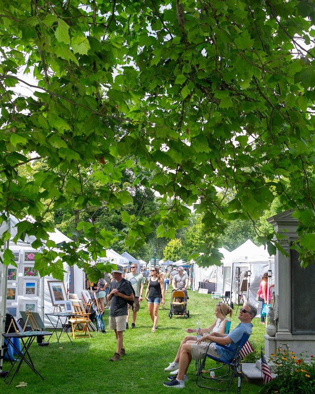 Shoppers and artwork booths set up on the lawn under shade trees at the New Milford Arts Festival