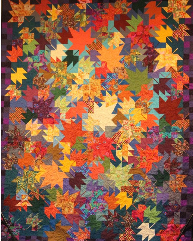 A quilt of autumn maple leaves in orange, red and gold on a dark patterned ground