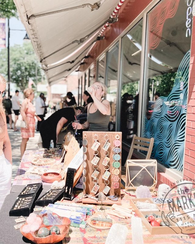 Shoppers at a market booth with jewelry and goods on display under a striped awning