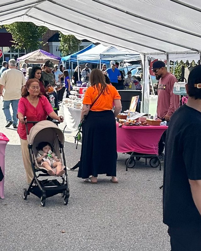 Shoppers browsing pink-draped vendor tables under white tents at the Greenleigh Fall Market.