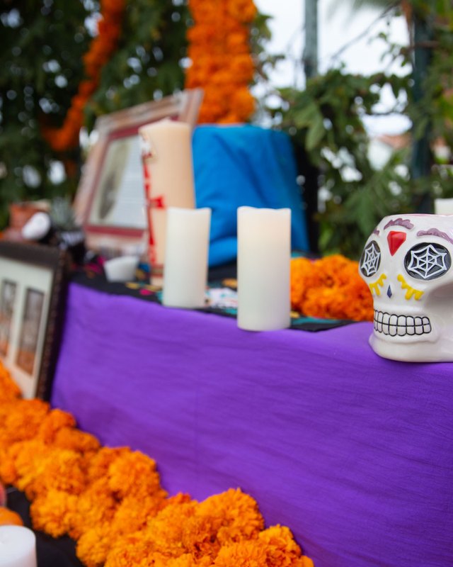 Dia de los Muertos ofrenda with candles, marigolds, sugar skull and framed photo on a purple altar.