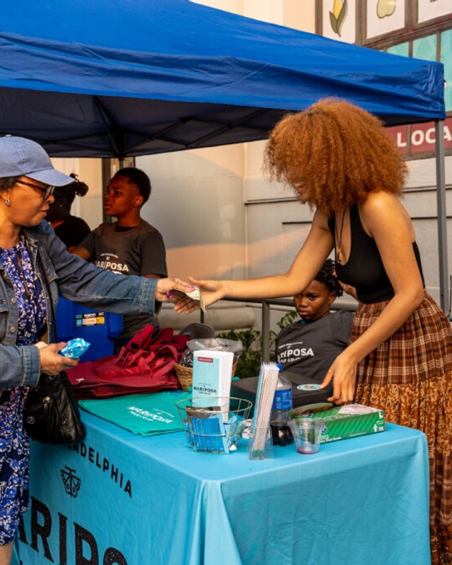 A guest visits a vendor at a blue-canopy booth during the Baltimore Avenue Dollar Stroll.