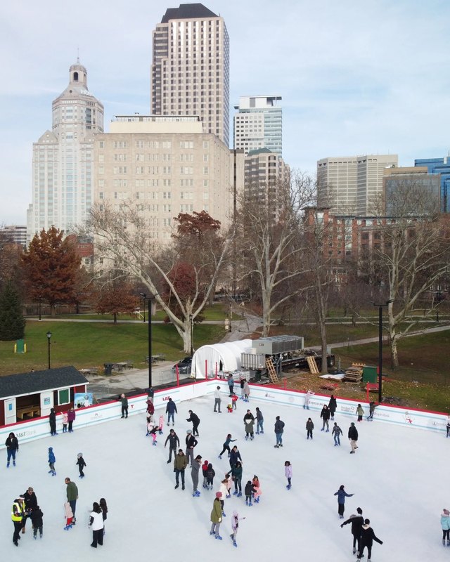 Skaters circling the outdoor rink in Bushnell Park with Hartford's downtown towers behind