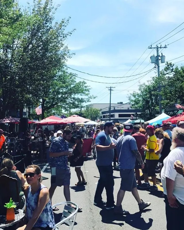 Crowd of people walking past tents and umbrellas at a sunny street festival in Bay Shore