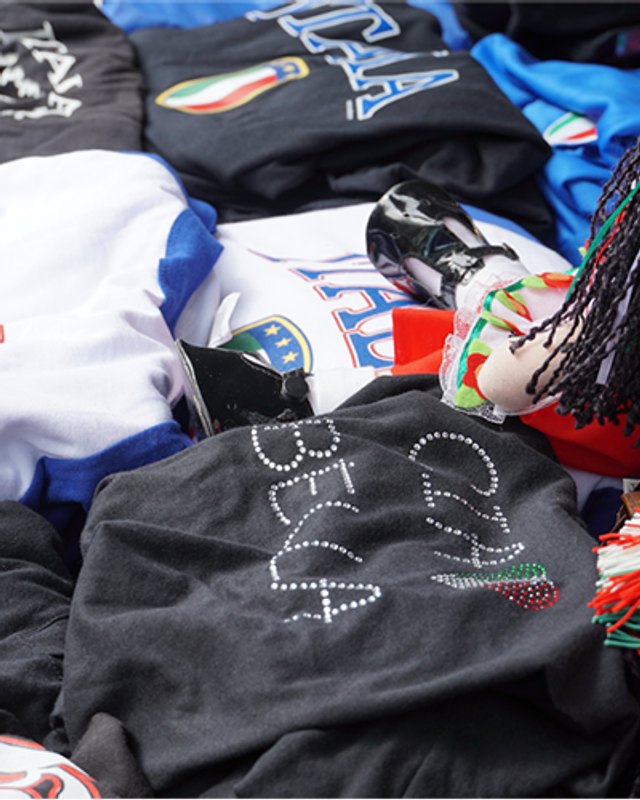 Italian-themed festival shirts and rhinestone tees piled on a merchandise table
