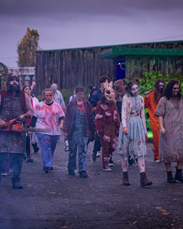 Costumed actors walking in a group in front of a fairground building at dusk