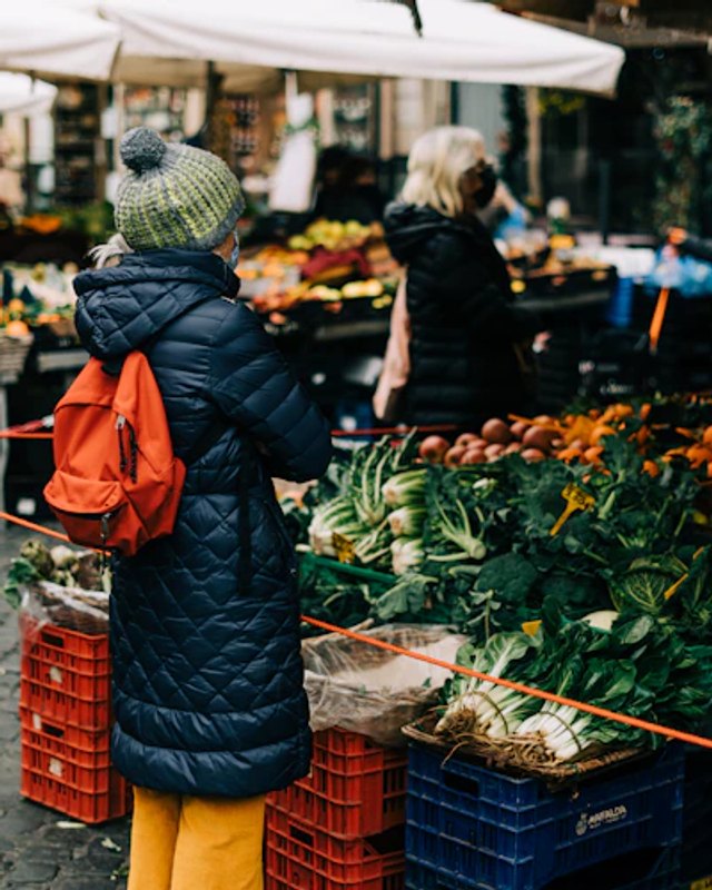 Shoppers browsing produce crates and market stalls at an outdoor farmers market.