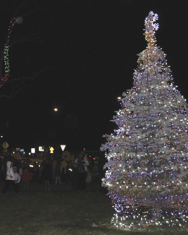 Crowd gathered at night under a tall lighted Christmas tree and holiday light displays in Kuna.