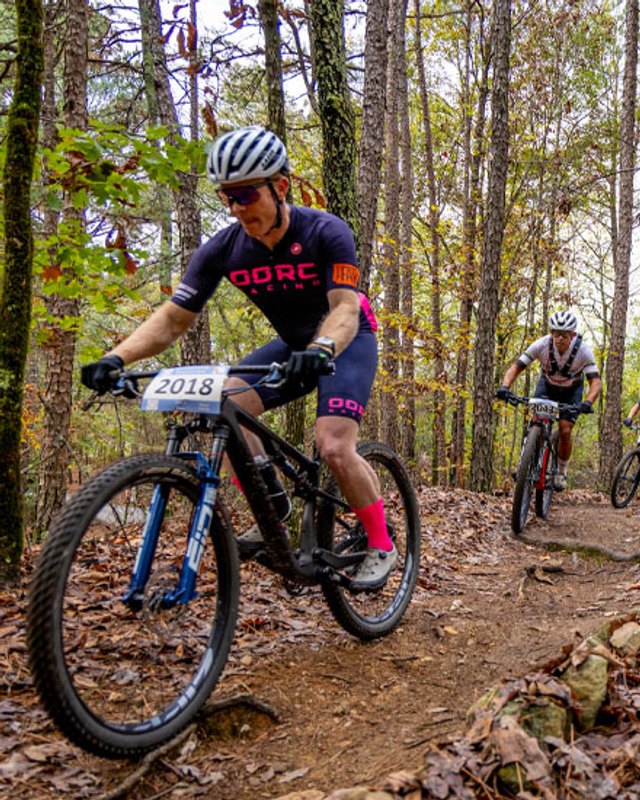 Mountain bikers riding a dirt trail through autumn woods at the Gudrun festival.