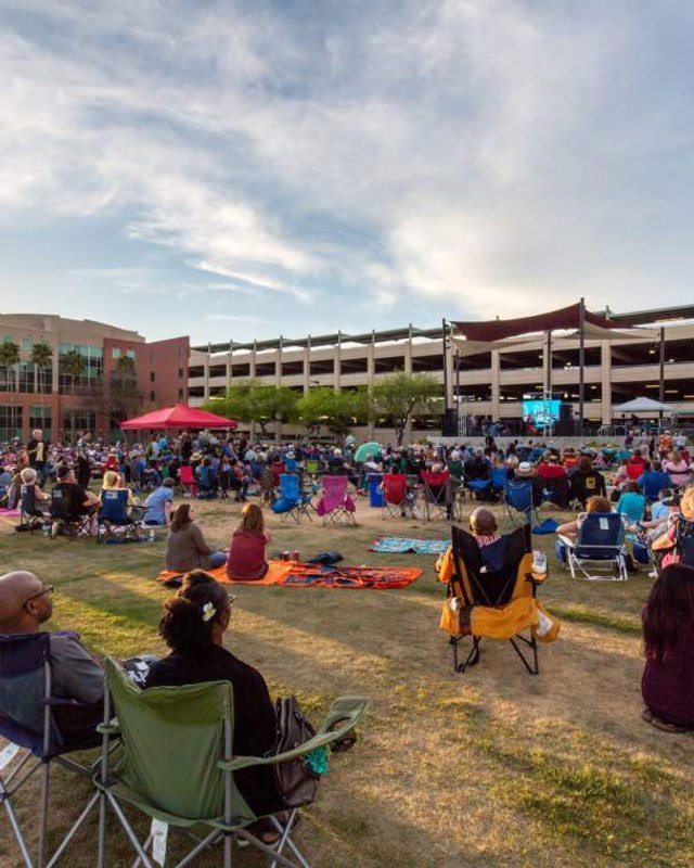 Crowd seated on lawn chairs in front of a stage at dusk at a Chandler park event.