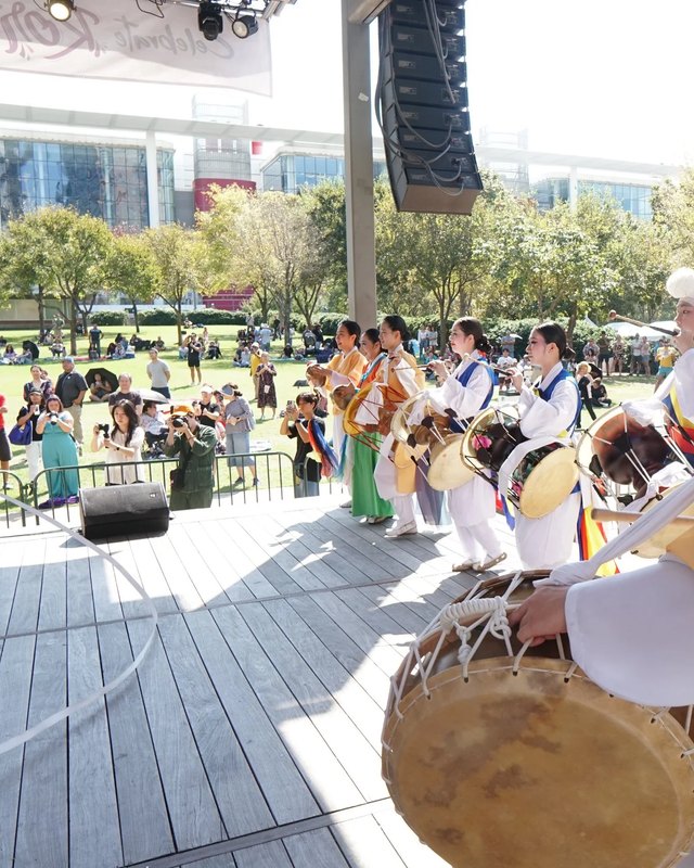 Traditional Korean drummers performing at Korean Festival Houston in a plaza with a crowd behind them.
