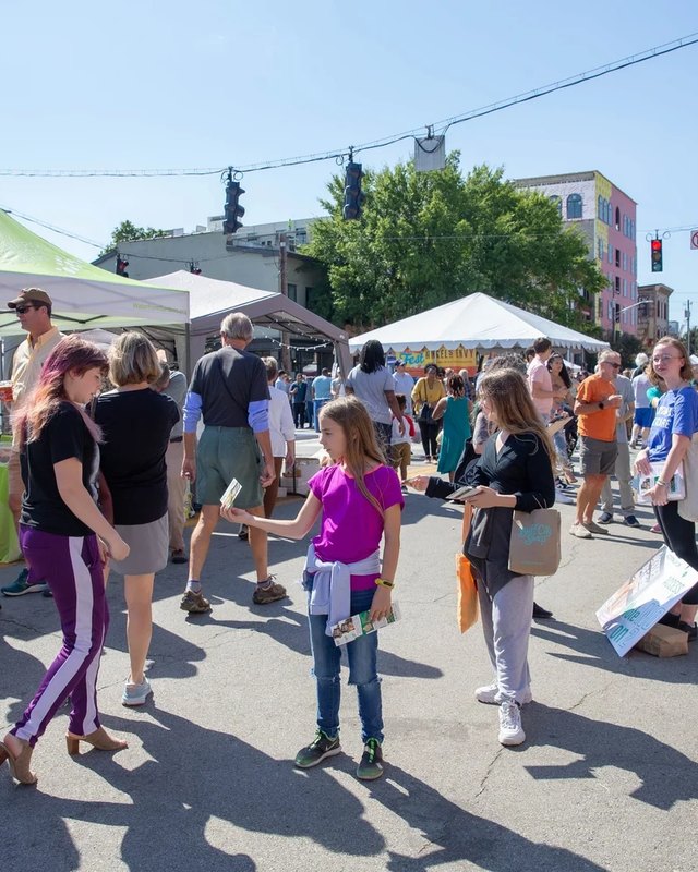 Crowds walking past white vendor tents on a sunny street during the NuLu Jingle Fest