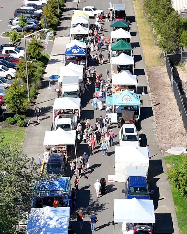 Aerial view of a busy market street lined with booth tents, mostly white with some green and blue, and shoppers walking between them.