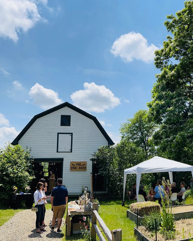Shoppers gathered at a white canopy tent and market tables in front of the white barn at The Vine Barn.
