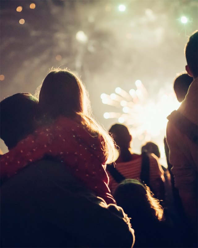 Silhouetted crowd watching bright fireworks burst at a July 4th celebration at night.