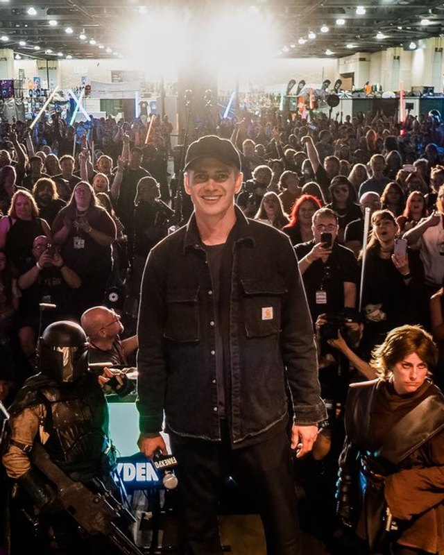 Crowd of cosplayers and fans in a convention hall at Fan Expo Philadelphia, with a man in dark shirt in the center.