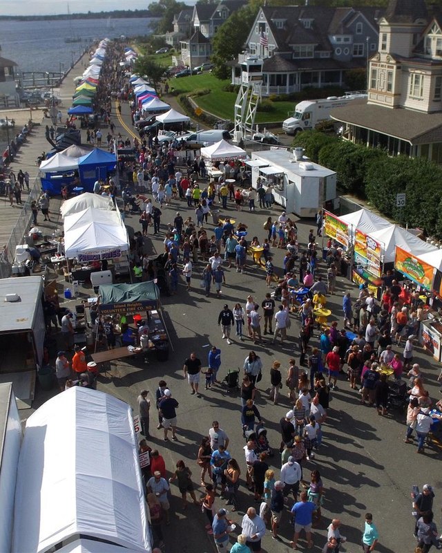 Aerial view of a crowded Sailfest waterfront with white vendor tents and shoppers along the street.