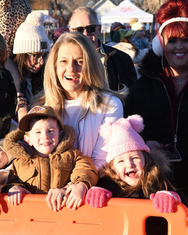 Smiling crowd of families and children behind an orange barrier at a winter outdoor event with tents in the background.
