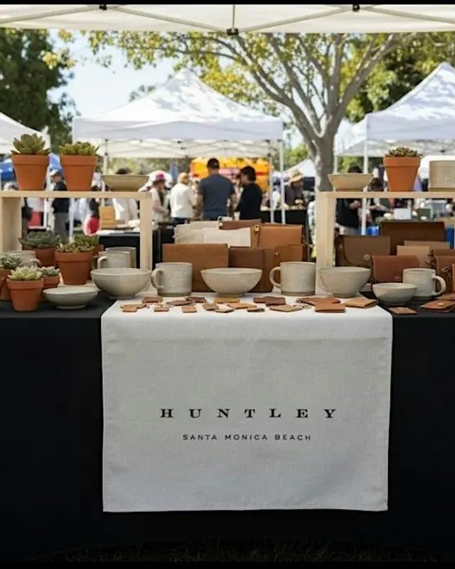 Huntley branded table of ceramic bowls and planters at an outdoor market tent with shoppers behind it