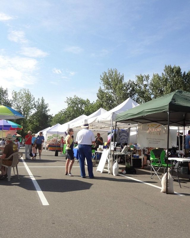 Shoppers and vendor tents at an outdoor farmers market on a sunny day in Golden