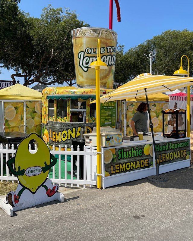 Lemonade stand with a lemon mascot and yellow tents at the Upland Lemon Festival