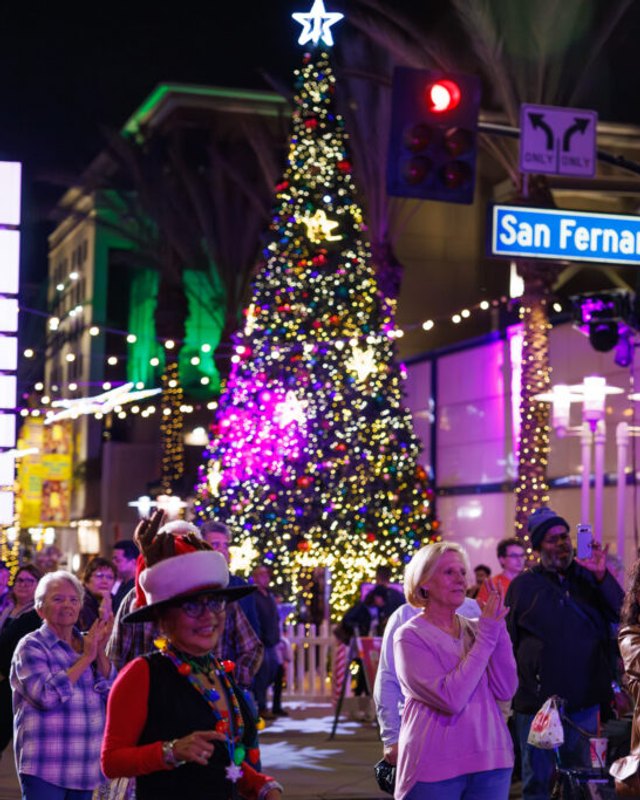 Festive crowd on San Fernando street in downtown Burbank beside a lit Christmas tree at night