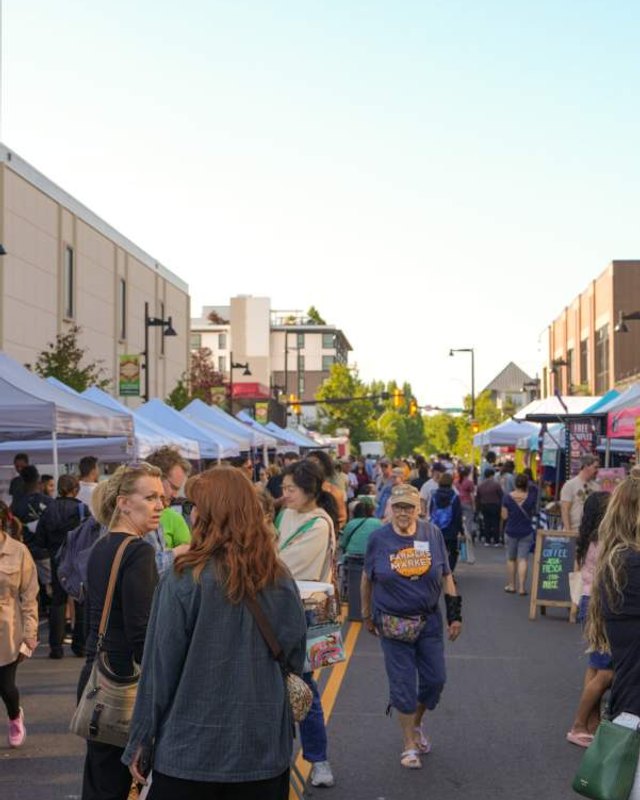 Shoppers walking along a sunny street lined with market tents and buildings