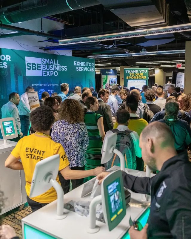 Attendees crowding exhibitor service desks at the Small Business Expo with staff in yellow shirts