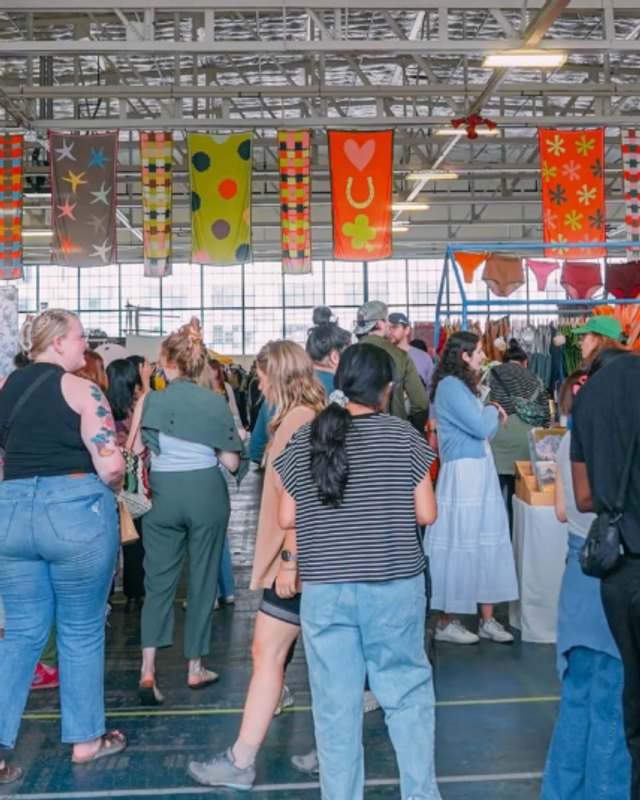 Crowd of shoppers browsing booths under hanging textile banners at a Renegade craft fair