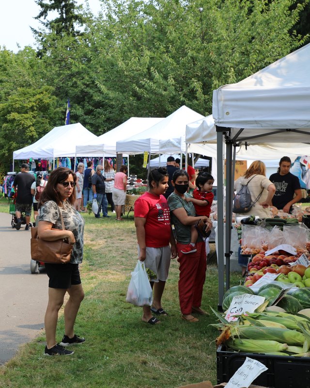 Shoppers browsing produce booths under white tents at the Auburn Farmers Market