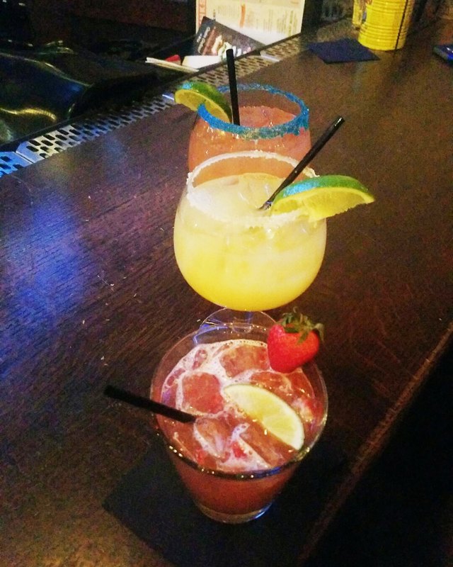 Two colorful rum cocktails with lime and strawberry garnish on a bar counter