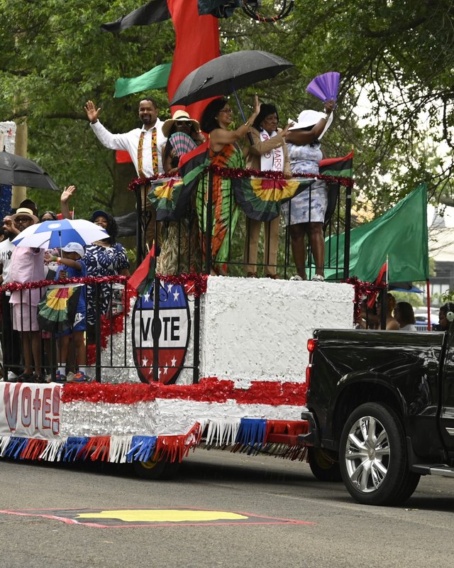 Parade float with a VOTE sign and people waving flags and umbrellas during the Juneteenth parade.