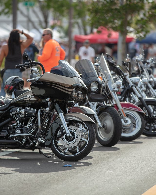 Rows of parked motorcycles along a street with spectators and tents behind them at Cape Coral Bike Night.