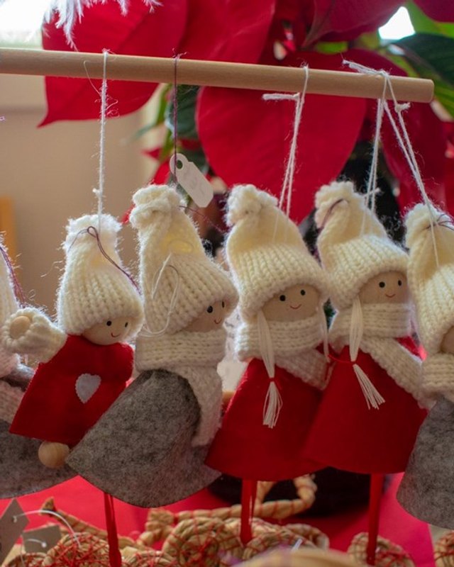 Handmade felt and knitted Christmas doll ornaments with white hats and red dresses hanging at a holiday craft display