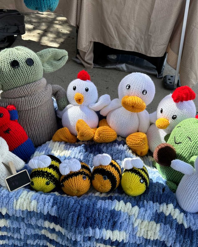Knitted toy animals and bees displayed on a blue knit blanket at a craft table.