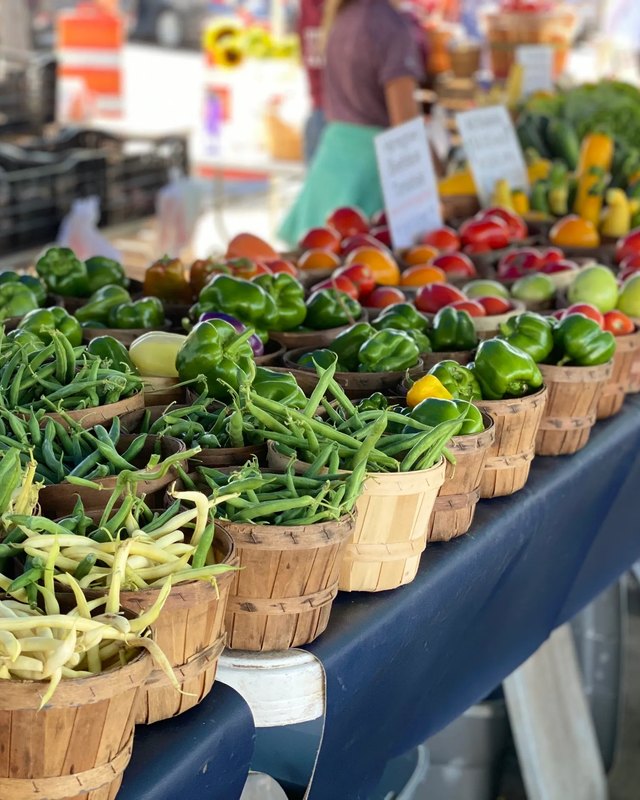 Baskets of green peppers, green beans and red and yellow peppers on a blue market table at a farmers market.